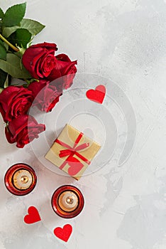 St. Valentine`s Day background. Small hearts, candles, a gift box and red roses bouquet on light concrete background. Romantic