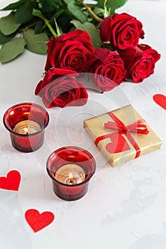 St. Valentine`s Day background. Small hearts, candles, a gift box and red roses bouquet on light concrete background. Romantic