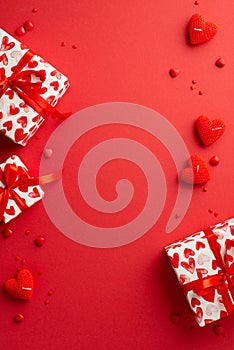 St Valentine`s Day concept. Top view vertical photo of gift boxes heart shaped candles and sprinkles on isolated red background