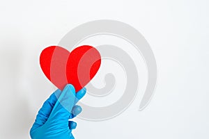 St. Valentine`s Day during the coronavirus pandemic. Blue latex glove hand holding red heart shape