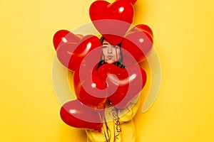 Woman`s face hiding between red balloons on yellow background.