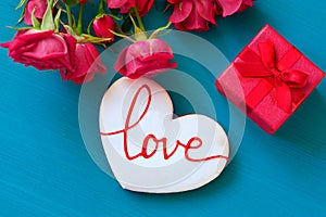 St. Valentines Day concept. Fresh red roses and gift box and gingerbread with the inscription love on wooden table. Top