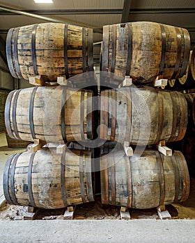 A stack of 6 traditional full whisky barrels, set down to mature, in a large warehouse