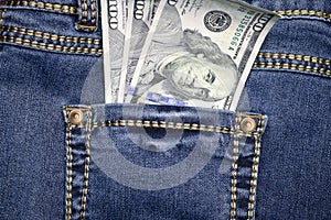 A stack of American hundred dollar bills in the back pocket of blue jeans. Money in your pocket, cash