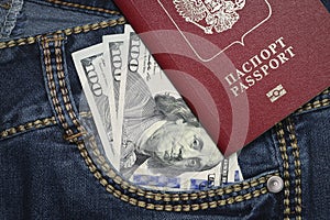 A stack of American hundred dollar bills in a pocket of blue jeans and an international passport of the Russian Federation. Money