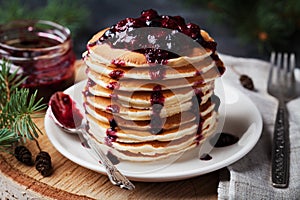 Stack of american pancakes or fritters with strawberry and blueberry jam in white plate on wooden rustic table decorated Christmas