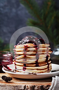 Stack of american pancakes or fritters with strawberry and blueberry jam in white plate on wooden rustic table decorated Christmas