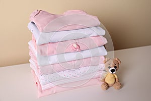Stack of baby girl`s clothes and toy bear on white table