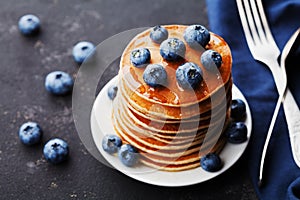 Stack of baked american pancakes or fritters with blueberries and honey syrup on rustic black background. Delicious dessert.