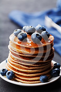Stack of baked american pancakes or fritters with blueberries and honey syrup on rustic dark table. Delicious breakfast.