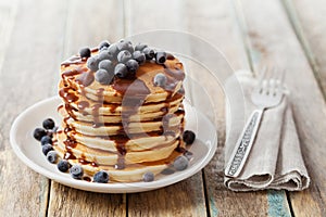 Stack of baked pancakes or fritters with chocolate sauce and frozen blueberries in a white plate