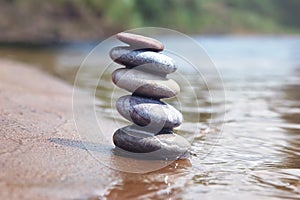 Stack of balancing pebble stones on sand and water edge as zen symbol