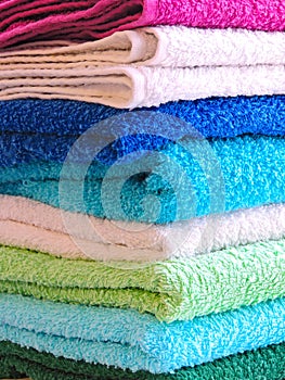 Stack of bath towels on light wooden background closeup.Pile of rainbow colored towels.Top view.