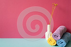 Stack of bathroom shower towels with vase of dry flower on skyblue shelf. pink wall background