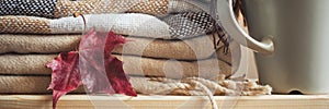 Stack of beige checkered wool blankets, autumn maple leaf and cup on a wooden chest.