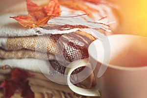 Stack of beige checkered wool blankets, cup and maple leaf on a wooden chest. autumn concept