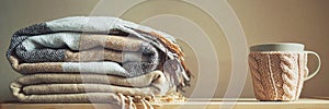 Stack of beige checkered wool blankets and cup on a wooden chest. autumn concept