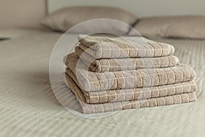 Stack of beige hotel towel on bed in bedroom interior.