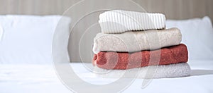 Stack of beige wool Sweaters on bed in luxury hotel or resort or home. Relax, autumn or winter clothes, laundry and vacation