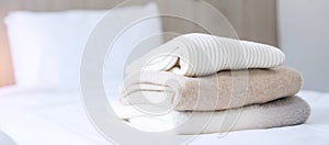 Stack of beige wool Sweaters on bed in luxury hotel or resort or home. Relax, autumn or winter clothes, laundry and vacation