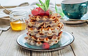 Stack of belgian waffles with honey, mint and fresh raspberries on turqouise plate