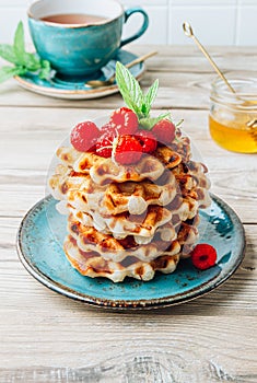 Stack of belgian waffles with honey, mint and fresh raspberries on turqouise plate