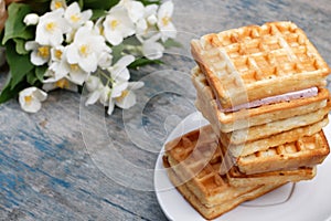 A stack of Belgian waffles on a white plate, on a wooden painted background.