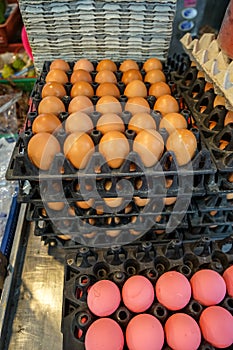 Stack of black trays full of natural light brown chicken eggs and pink preserved eggs selling in local food market