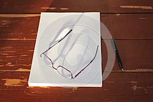 A stack of blank sheets of paper, a pen and glasses on a Red wooden table