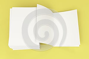 Stack of blank white closed and one open brochure mock-up on yellow backgroun