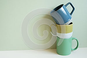 Stack of blue and green mug cups on white table. mint wall background. copy space