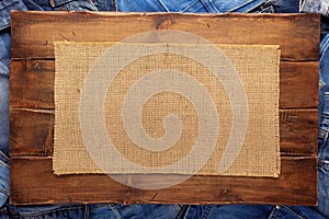 Stack of blue jeans denim and wood name plate. Jeans heap under sack hessian background