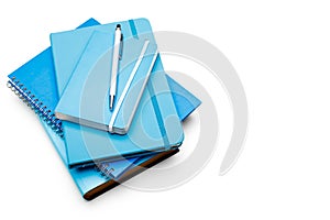 Stack of blue ring binder book and notebook with silver pencil on white background