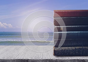 Stack of book and a holy bible on wooden table over sea and blue sky background