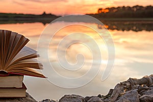 Stack of book and Open hardback book on blurred nature landscape backdrop against sunset sky with back light. Copy space, back to