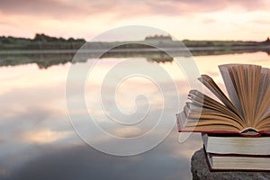 Stack of book and Open hardback book on blurred nature landscape backdrop against sunset sky with back light. Copy space, back to