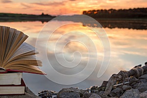 Stack of book and Open hardback book on blurred nature landscape backdrop against sunset sky with back light. Copy space, back to