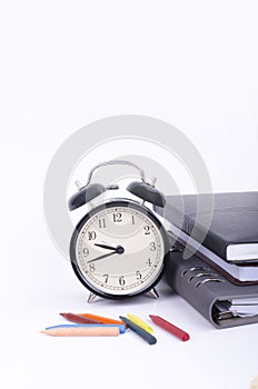 Stack of book with ticking vintage clock and colorful crayon on white table