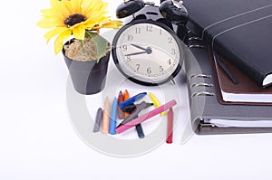 Stack of book with ticking vintage clock and colorful crayon on white table