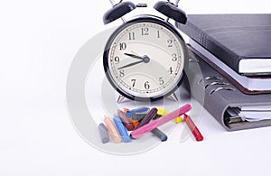 Stack of book with ticking vintage clock and colorful crayon on white table