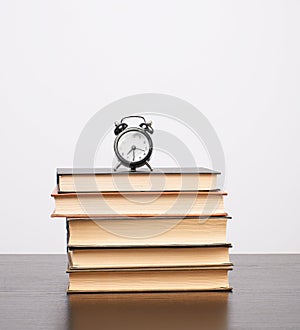 stack of books and a black alarm clock on the table
