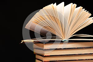 Stack of books on black background, open book.