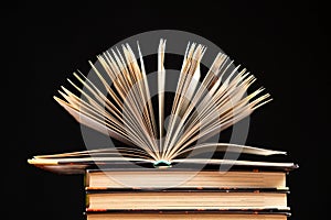 Stack of books on black background, open book.