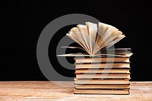 Stack of books on black background, open book, space for text.