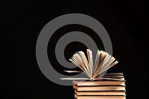 Stack of books on black background, open book, space for text.