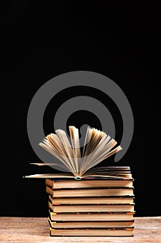 Stack of books on black background, open book, space for text.
