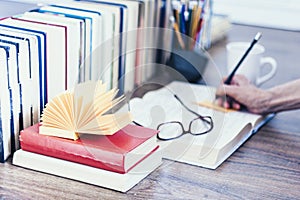 Stack of books education background, open book, female hand with pencil, glasses, and cup of tea with lemon
