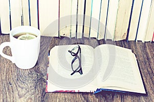 Stack of books education background, open book, glasses, and cup of tea with lemon