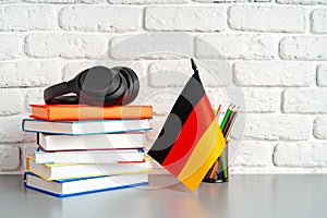 Stack of books and flag of Germany on desk. German language learning concept