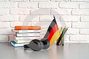 Stack of books and flag of Germany on desk. German language learning concept